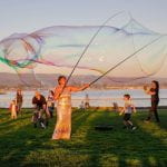 An outdoor art installation featuring an artist creating giant bubbles